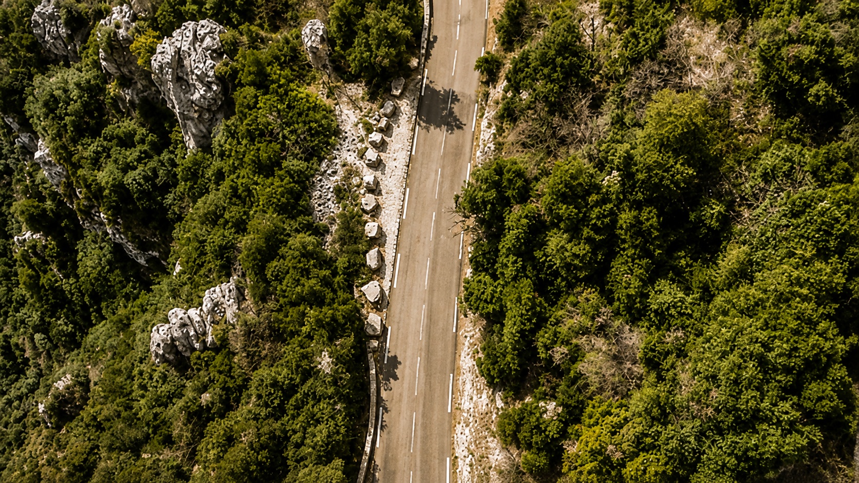Aerial view of a winding mountain road surrounded by dense forest and rocky terrain.
